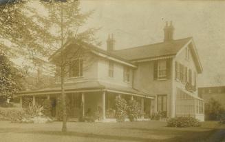 Black and white photograph of a three story house with a large front verandah.
