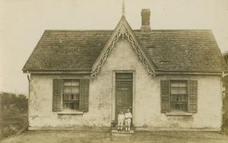 Black and white photograph of two children standing on the step of a small bungalow.