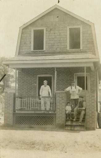 Black and white photograph of three men and a boy standing on the porch of a two story brick ho ...