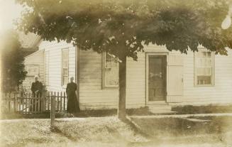 Black and white photograph of two women standing in front of a small, frame bungalow.