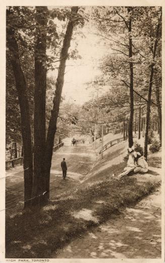 Sepia toned photograph of people sitting on a grassy hill beside a country road.