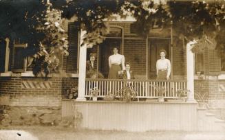 Black and white photograph of three women and a man standing on the verandah of a brick home.