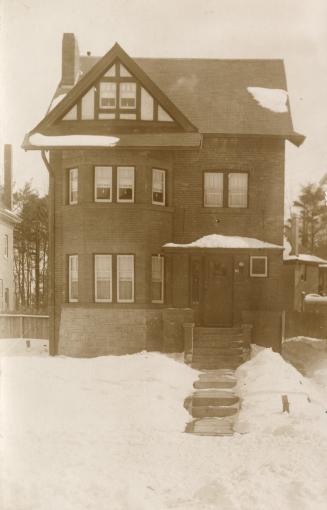 Black and white photograph of a of a three story house with snow on the ground.