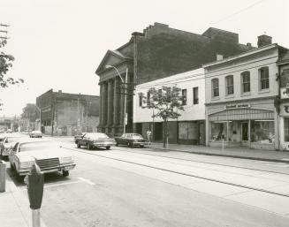 Picture of street scene with large library buildings and shops and streetcar tracks and cars. 