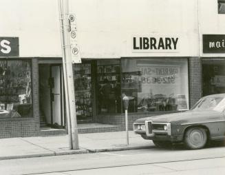 Picture of street scene with parked car and storefront with sign saying Library. 