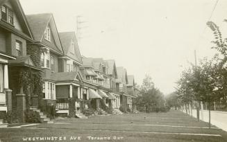 Black and white photograph of three-story houses and trees lining a street.