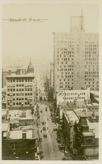 Black and white photograph of large buildings on a downtown street, taken from the air.
