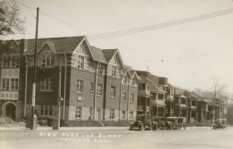 Black and white photograph of cars parked beside a sidewalk lining a row of newly build townhou ...