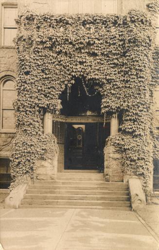 Black and white photograph of the ivy covered entrance to a very large late Victorian design bu ...