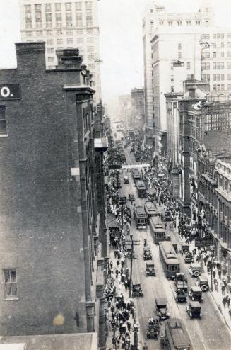 A photograph of a paved city street, taken from a high vantage point. There are cars and street ...