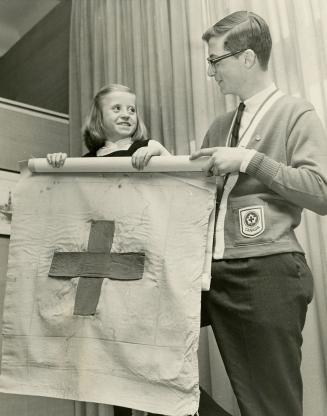 Picture of teenage boy and young girl standing holding flag with cross on it. 
