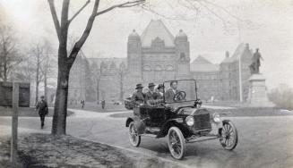 A photograph of four people in a car on a paved road with a large government building in the ba ...