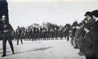A photograph of a military parade, with dozens of men wearing uniforms and pith helmets marchin…
