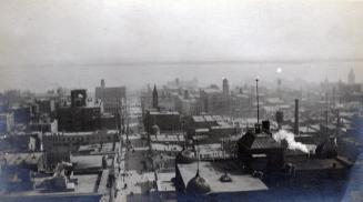 A photograph of a city skyline taken from a high vantage point, looking down at several city bl…