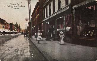 Colorized photograph of three ladies walking on the sidewalk outside of stores lining a downtow ...