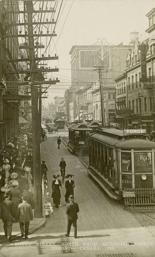 Black and white photograph of a very busy city street corner with automobiles and streetcars.
