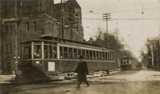 Black and white photograph of three streetcars running along a city street with a man waling in ...
