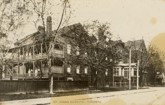 Black and white photograph of a large two story brick house with people standing on wooden balc ...