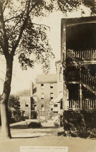 Black and white photograph of large two story brick houses with wooden balconies.