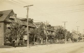 Black and white photograph of a row of similar three story houses on the left hand side of a ci ...