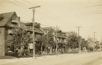 Black and white photograph of a row of similar three story houses on the left hand side of a ci…