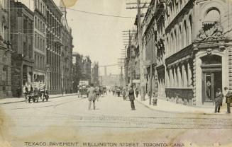 Black and white photo postcard depicting Wellington Street looking east from Yonge St. with bui ...