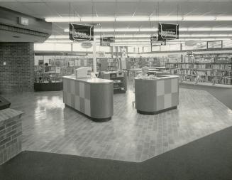 Interior view of library with reference desk and shelves of books. 