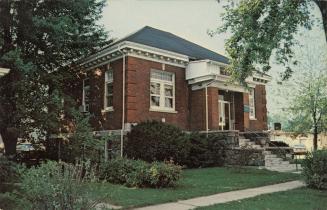 Picture of red brick library building with front lawn and trees. 