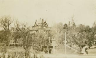 A photograph of two large two or three story houses on top of a small hill, with trees and shru ...