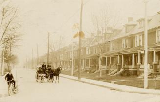 Black and white photograph of a row of similar three story houses on the left hand side of a ci ...