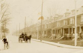 Black and white photograph of a row of similar three story houses on the left hand side of a ci…
