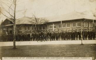 Black and white photograph of lines of servicemen in front of a one story building made of ceme ...