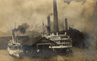 Black and white photograph of boats moored at a cover dock with a lot of smoke coming from smok ...