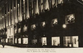 Black and white photograph of the front of a department store with banners at night with decora ...