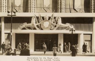 Black and white photograph of the entrance of a department store with a crest with the profiles ...