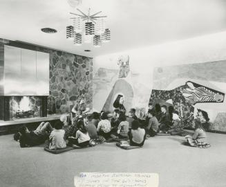 Picture of a librarian telling a story to a group of children in front of a fireplace with a la ...