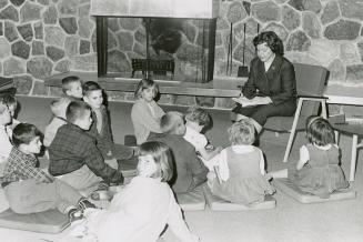 Picture of a librarian reading a book to a group of children seated on the floor. 