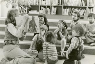Picture of a librarian reading a story book to a group of children. 