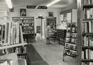 Picture of interior of library branch showing librarian at card catalogue and shelves of books. ...