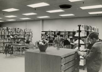 Picture of interior of library branch and man using card catalogue. 