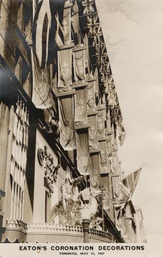 Black and white photograph of flags and statues decorating the outside of a department store.