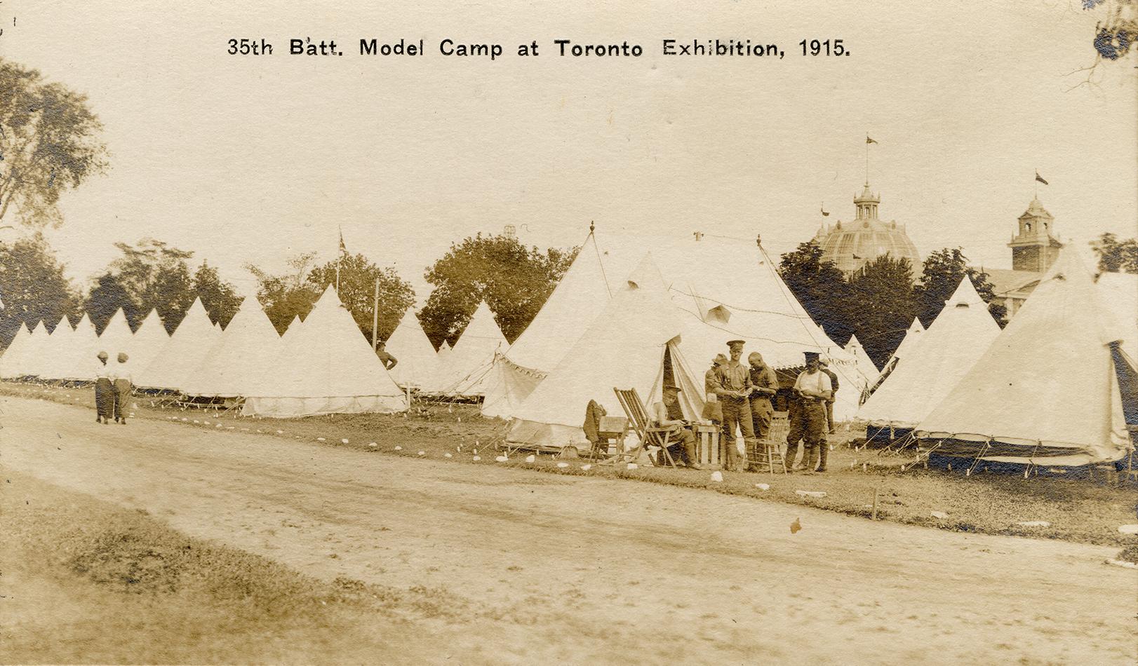 Black and white picture of soldiers standing in front of dozens of tents.
