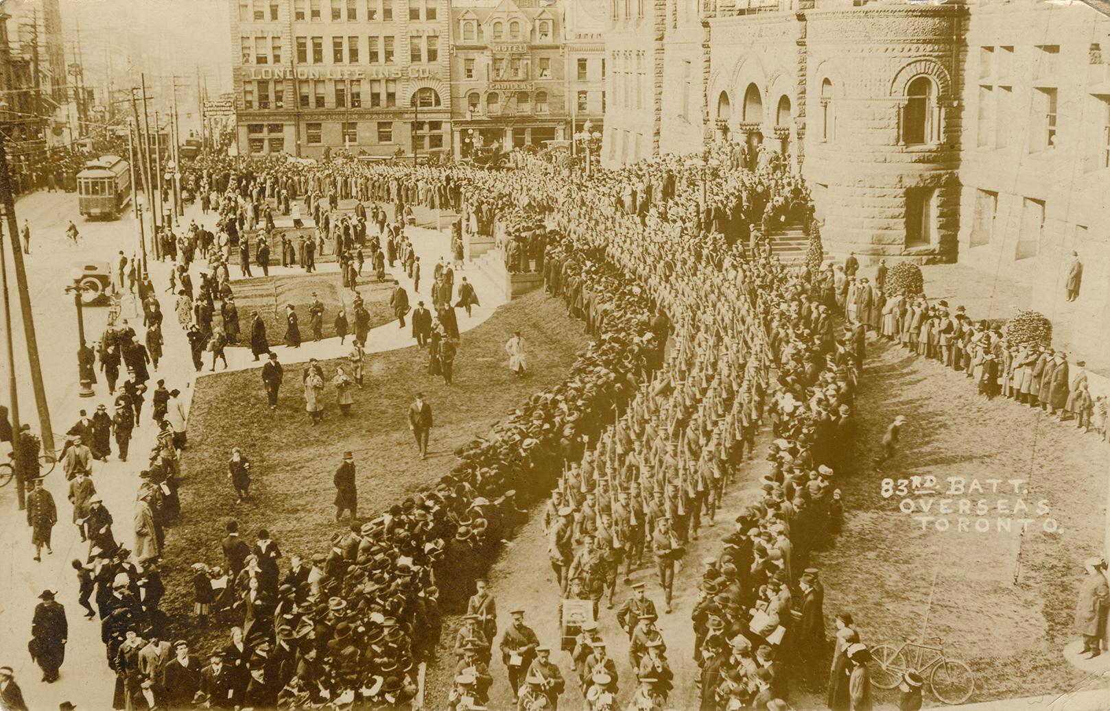 Black and white picture of soldiers marching in front of large, Richardsonian Romanesque buildi…