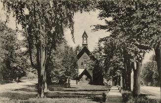 Black and white photograph of a frame church nestled amongst tall trees.