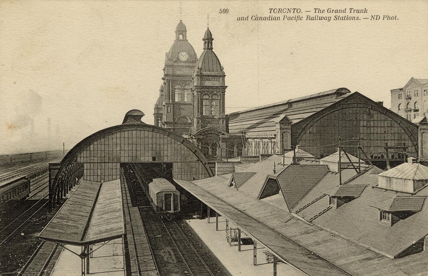 Black-white photo postcard depicting the exterior of a train station with the railroad yard, on ...