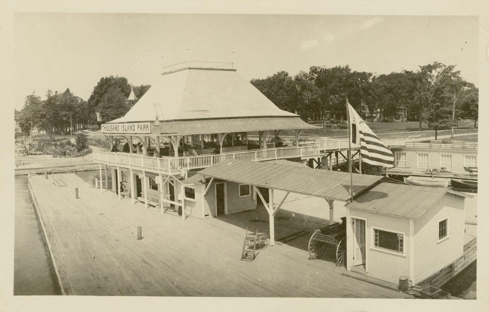 Black and white photograph of a two story covered structure beside a large dock in a river.