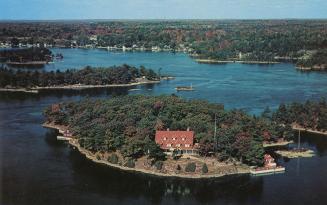 Colorized photograph of an island with a big house built on it in the middle of a river.