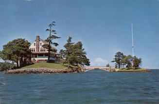 Colorized photograph of a view of a waterway, with a large home on an island connected by a sma ...