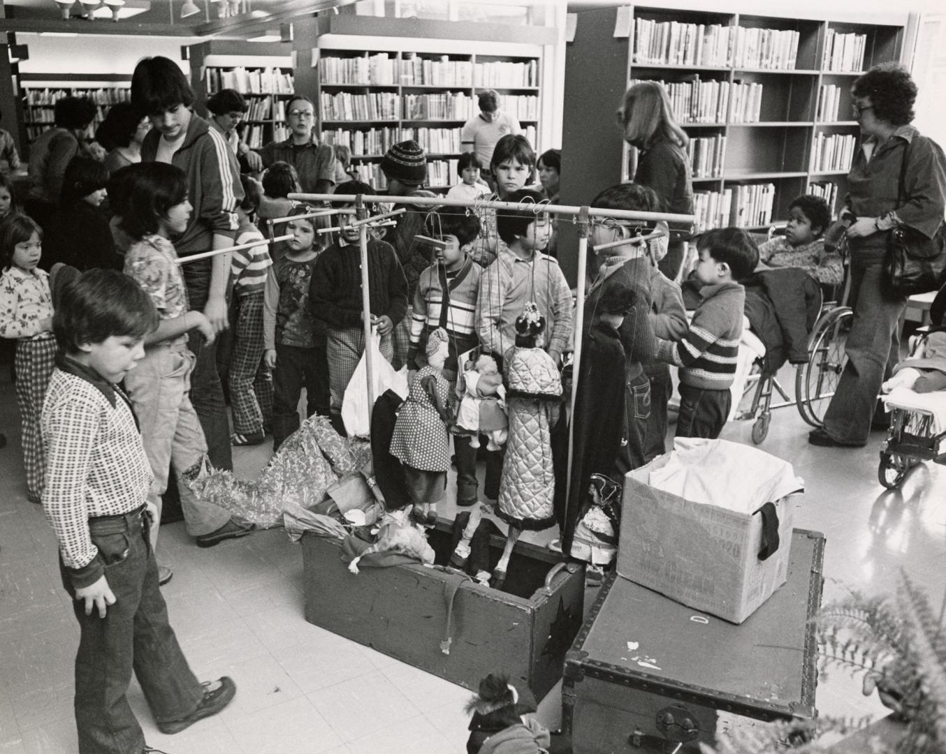 Picture of children looking at puppets in a library. 