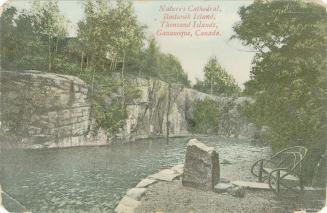Colorized photograph of a rattan chair on a river bank while a narrow river flows by.